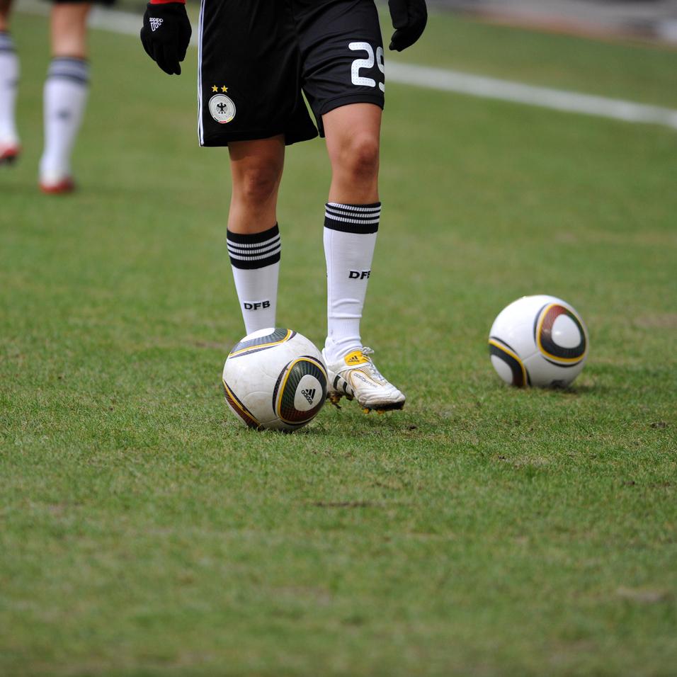 Nahaufnahme eines Fußballspielers mit einem Ball auf dem Rasen, im Hintergrund ein weiterer Ball.