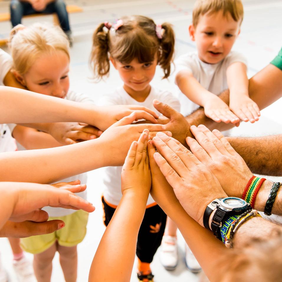 Kinder und Erwachsene legen ihre Hände in einem Kreis zusammen, symbolisieren Zusammenarbeit und Gemeinschaft.